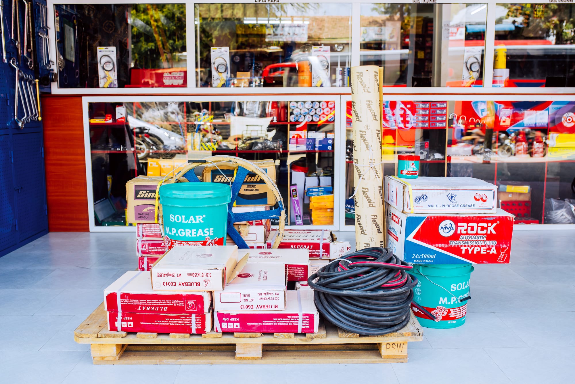 Pallet of boxed stock, grease buckets and hose coiled outside the Chasama showroom